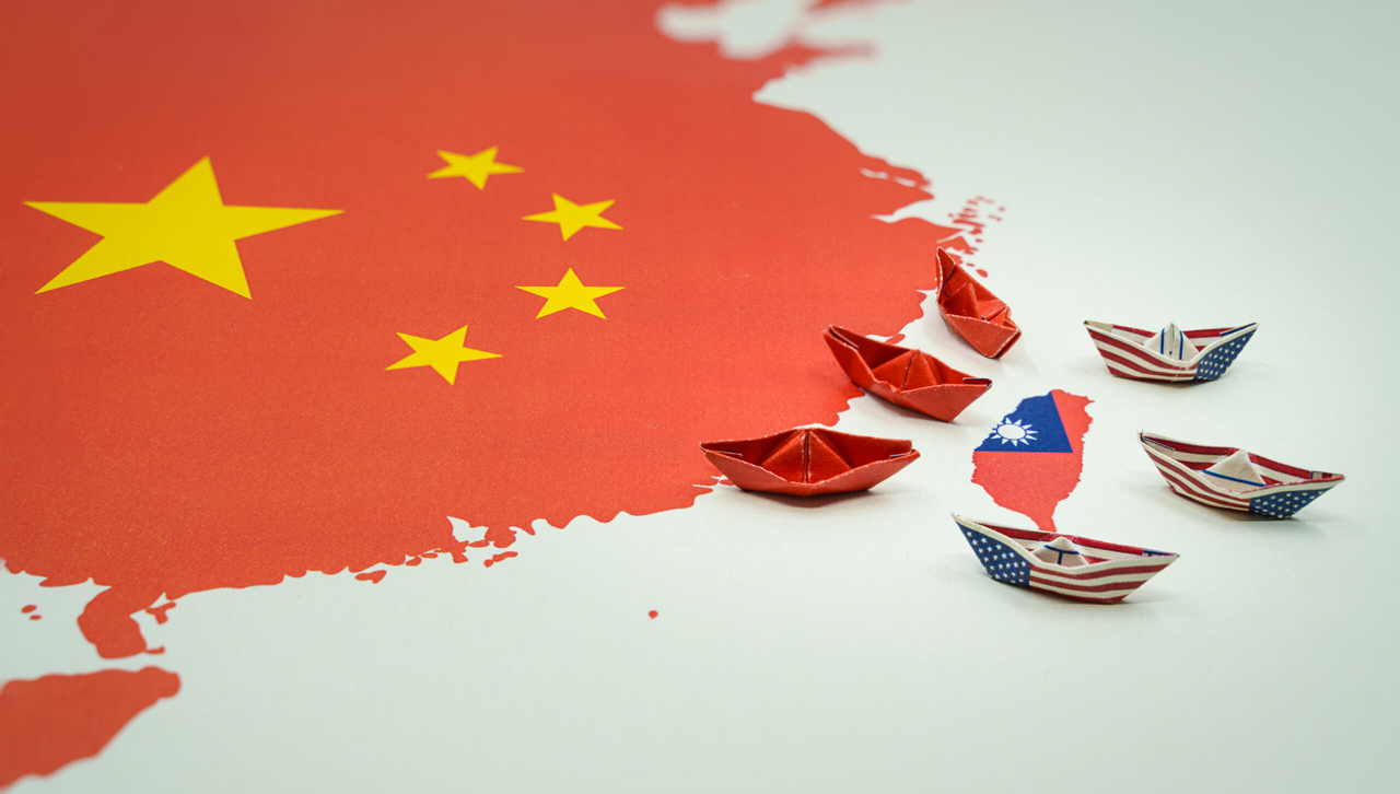 Paper boats with the colors of the USA and China surrounding the island of taiwan on a map