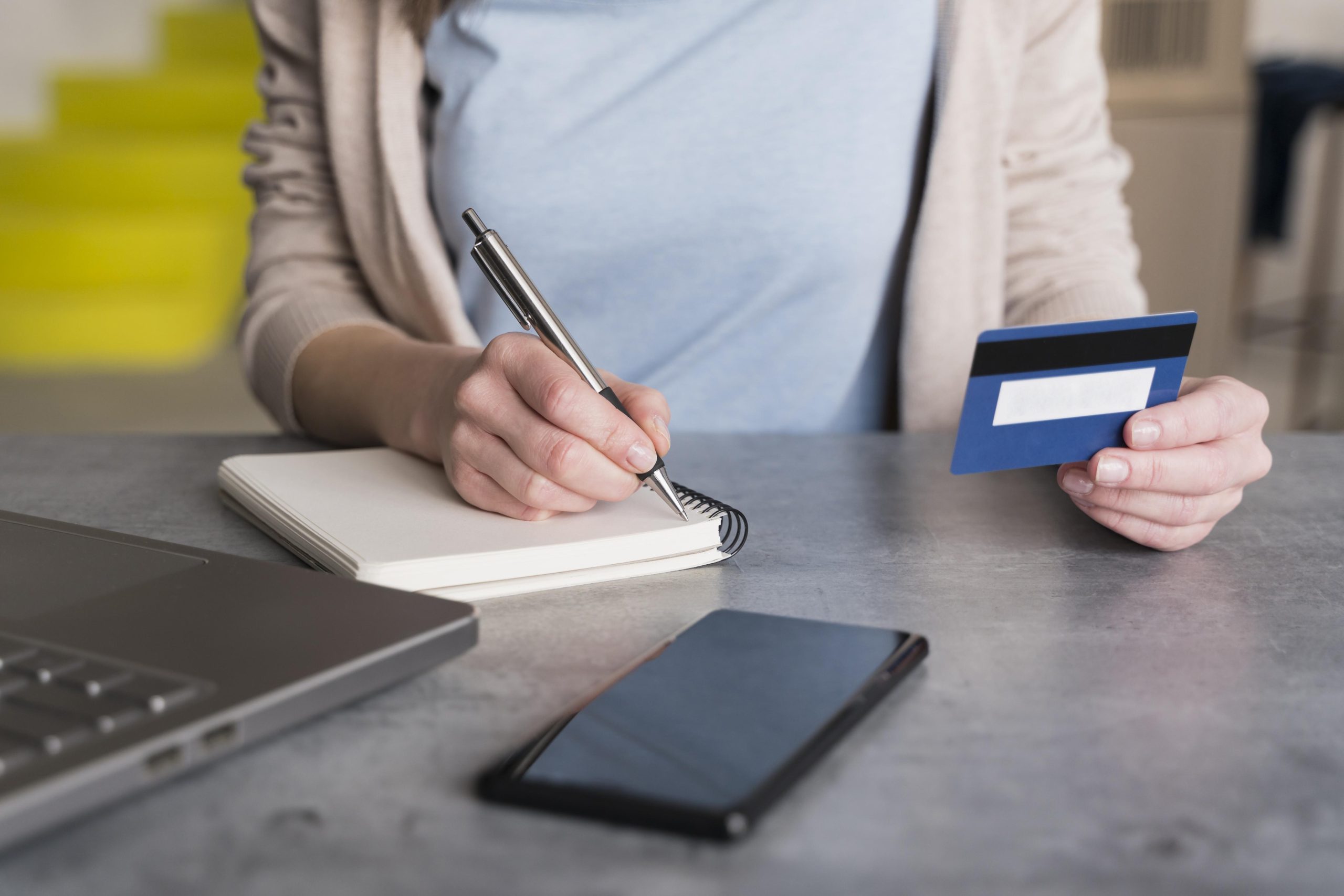 high-angle-woman-home-holding-credit-card-writing-notepad